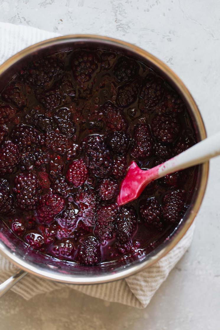 A saucepan filled with blackberry filling being stirred with a white spatula.