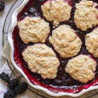 A baked blackberry cobbler in a round white baking dish.