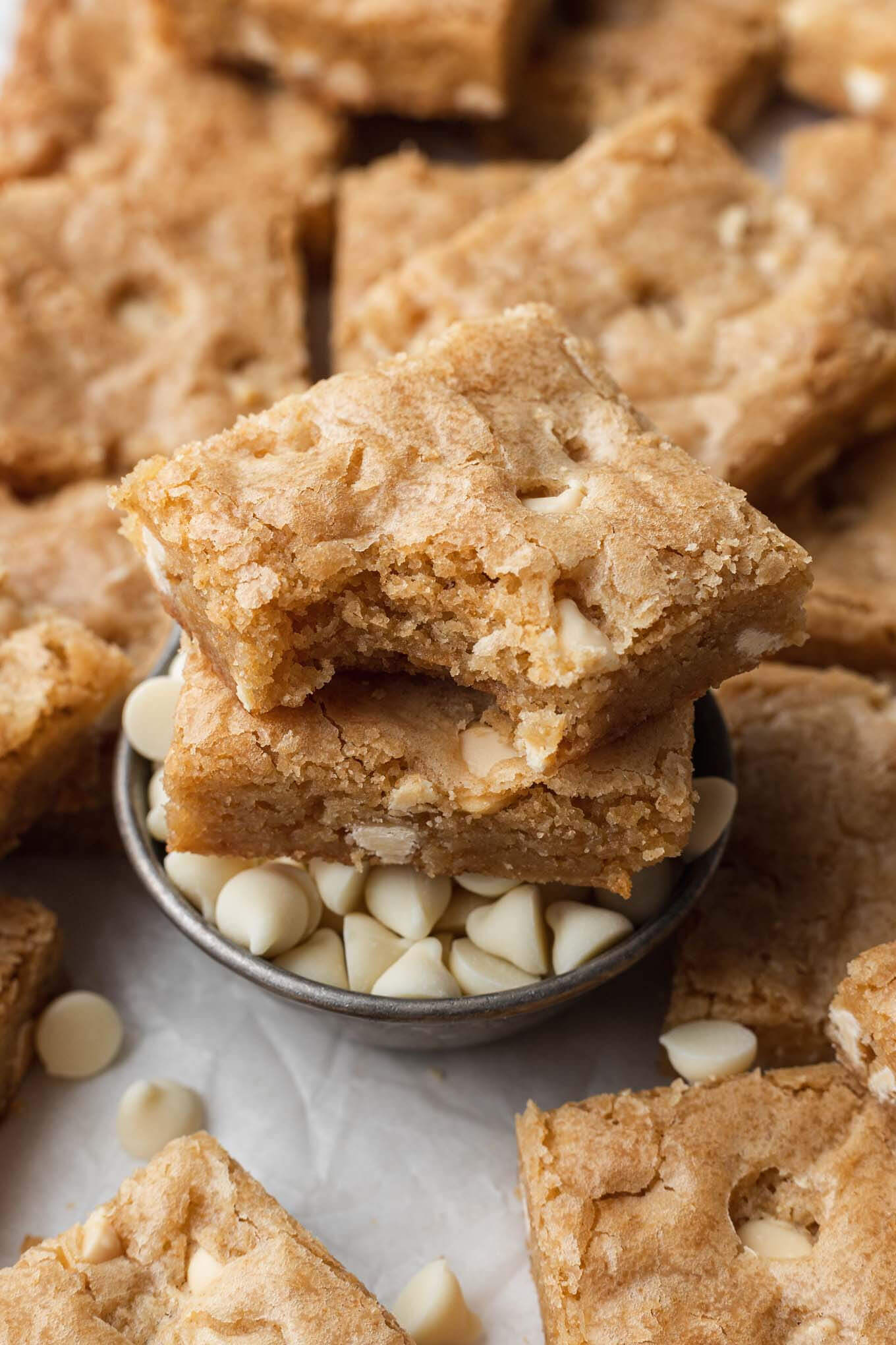 Two blondies (one with a bite missing) stacked atop a small dish of white chocolate chips. 