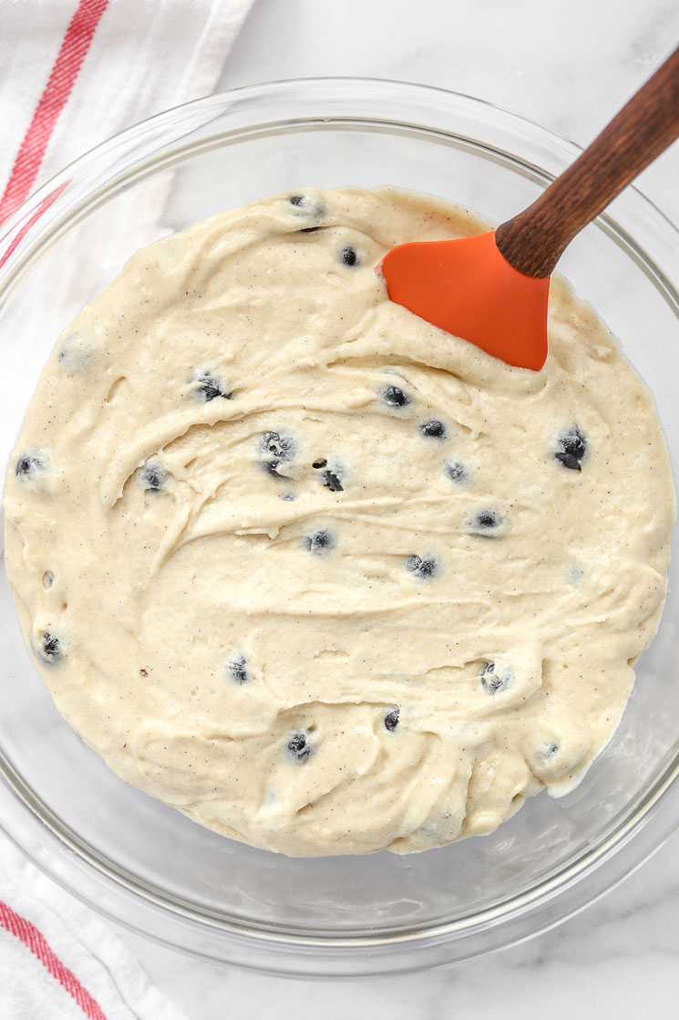 A glass bowl filled with blueberry muffin batter.