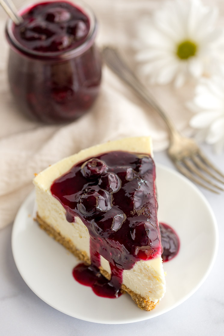 A slice of cheesecake topped with blueberry sauce on a white plate.