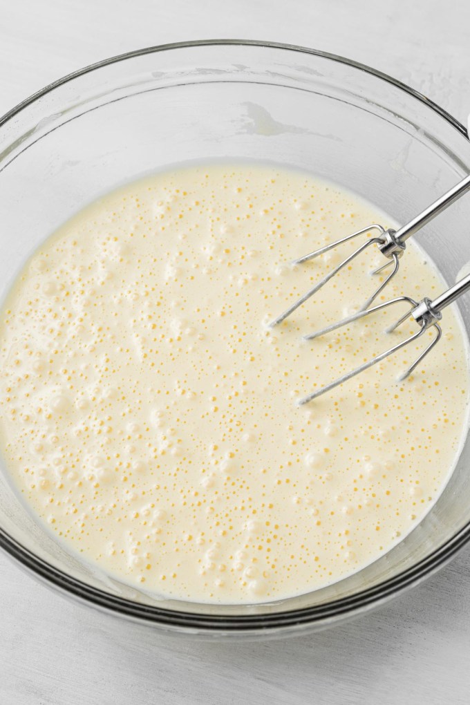 Sponge cake batter in a glass mixing bowl, with metal beaters leaning on the side.