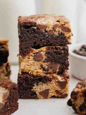 A stack of three brookies with more brookies and a small bowl of chocolate chips next to it.