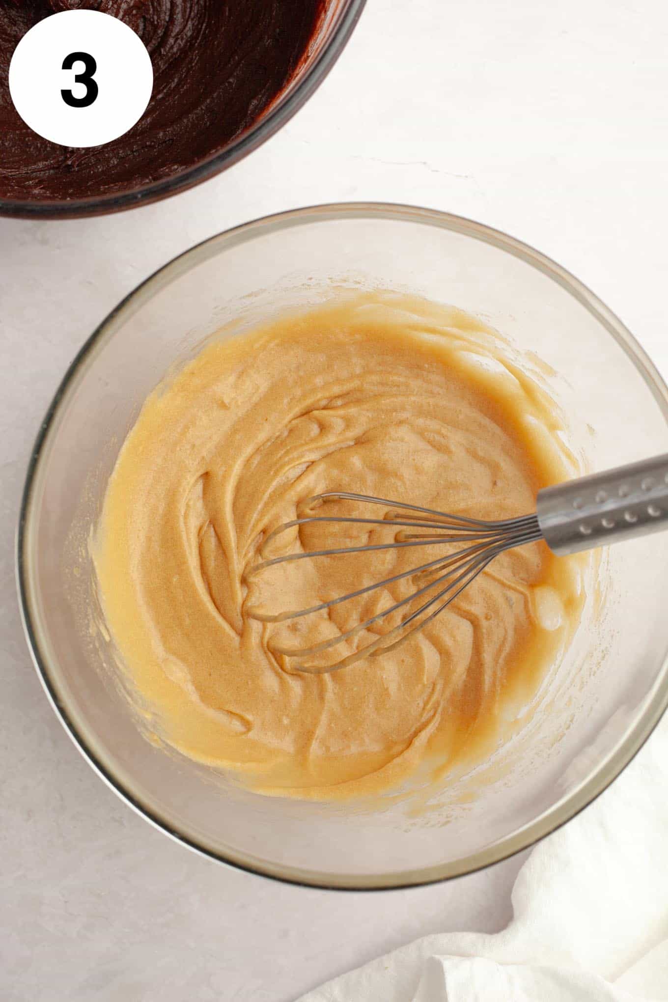 An overhead view of melted butter, eggs, and sugar in a glass mixing bowl, with a whisk. 