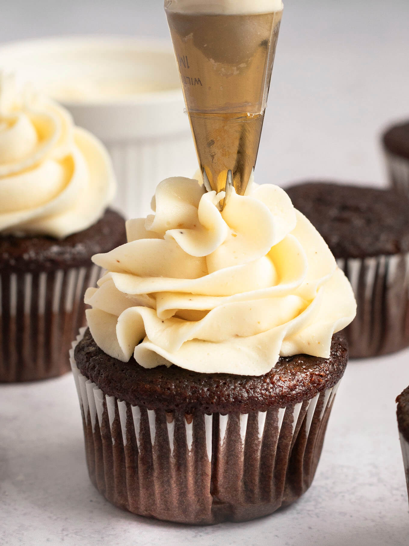 A chocolate cupcake with brown butter frosting being piped on top of it.