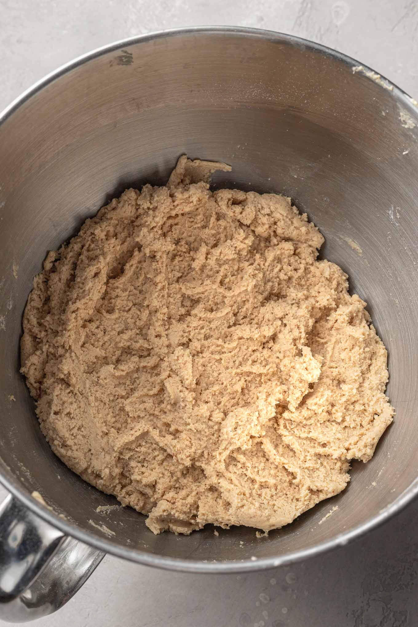 An overhead view of browned butter snickerdoodle cookie dough in a mixing bowl, with a paddle attachment. 