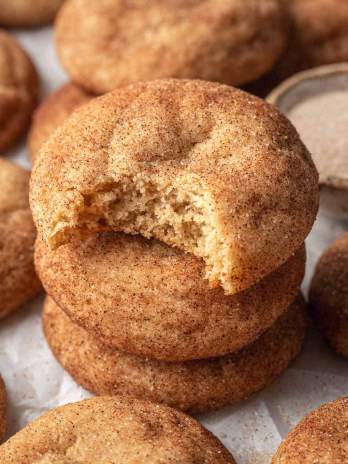 Three snickerdoodles stacked on top of each other. The top cookie has a bite missing.