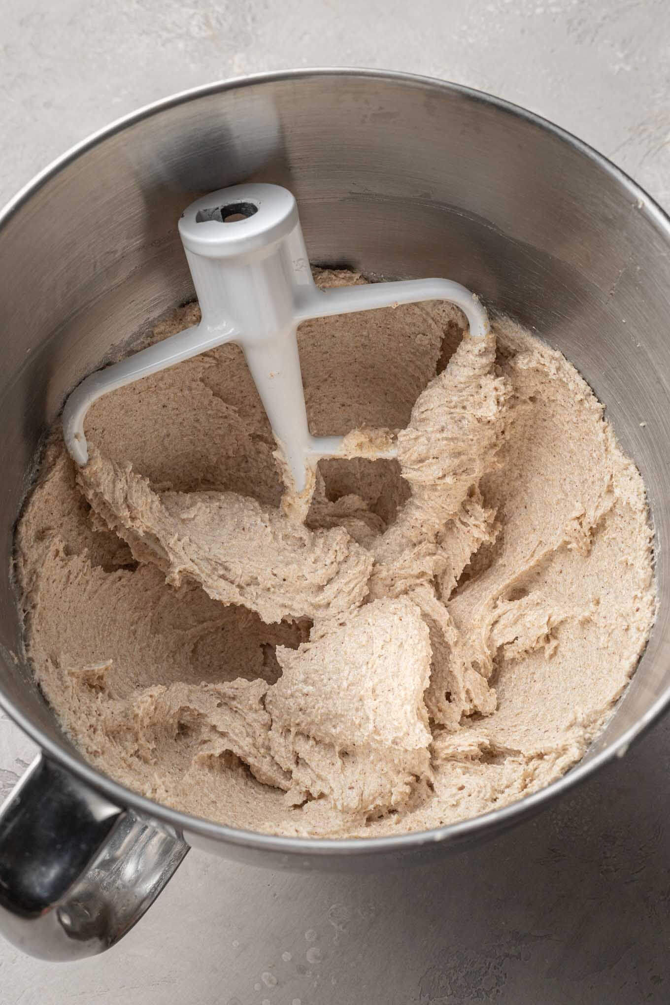 An overhead view of creamed brown butter and sugar in a mixing bowl, with a paddle attachment. 