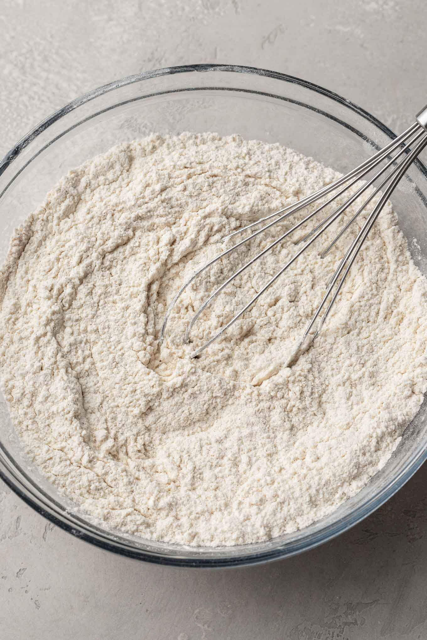 An overhead view of the dry ingredients needed for snickerdoodles in a mixing bowl, with a whisk. 