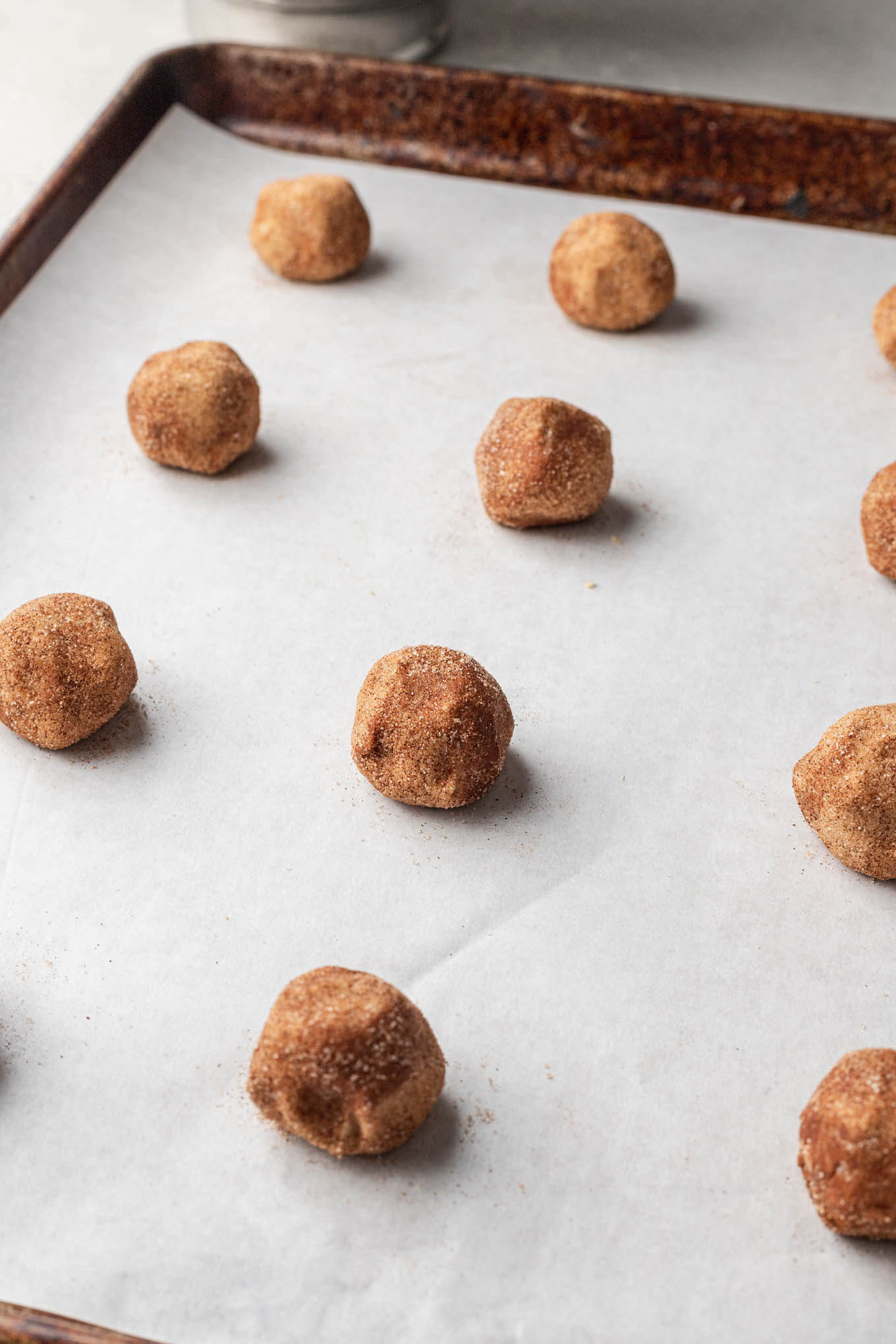 Raw brown butter snickerdoodle cookie dough balls on a parchment paper-lined baking sheet. 