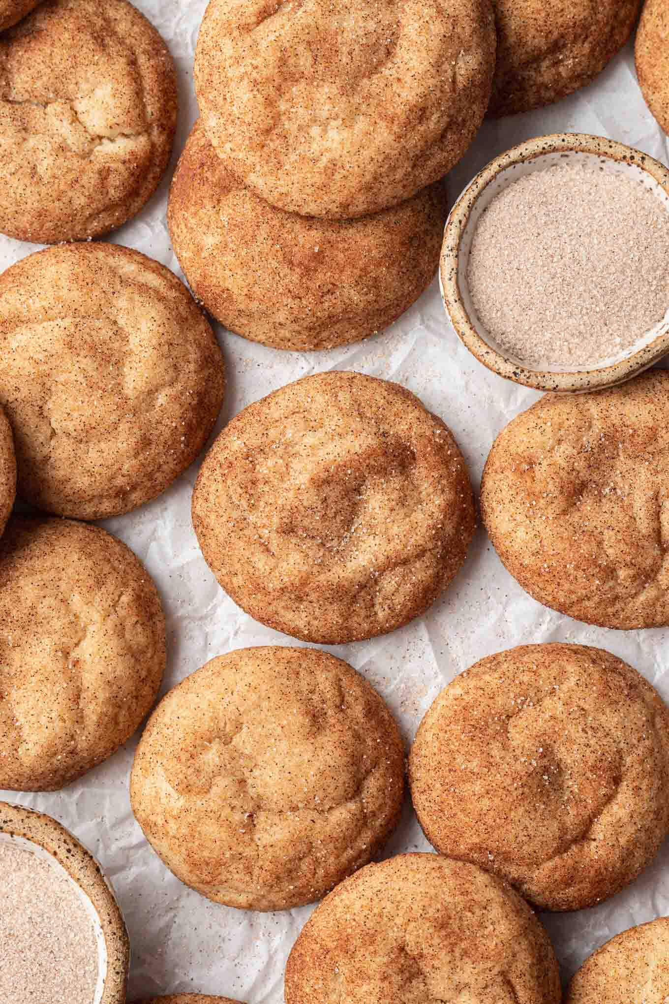 An overhead view of browned butter snickerdoodles on parchment paper, with a dish of cinnamon sugar on the side. 