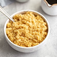 A bowl of light brown sugar with a spoon resting in it. A small container of molasses sits in the background.