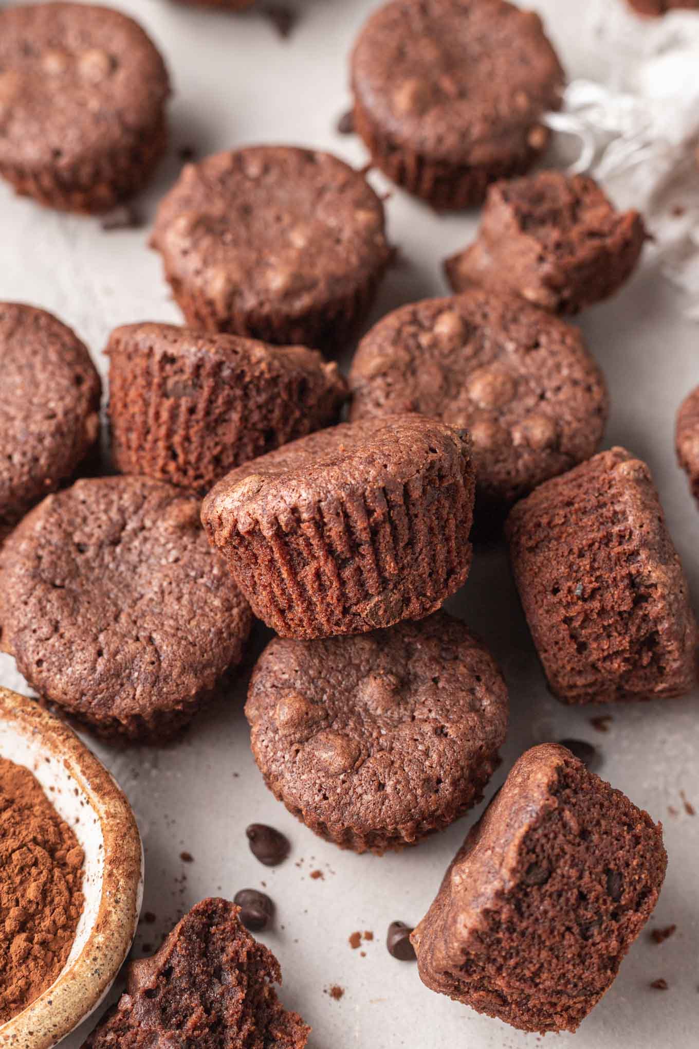 A pile of homemade brownie bites next to a dish of cocoa powder. 