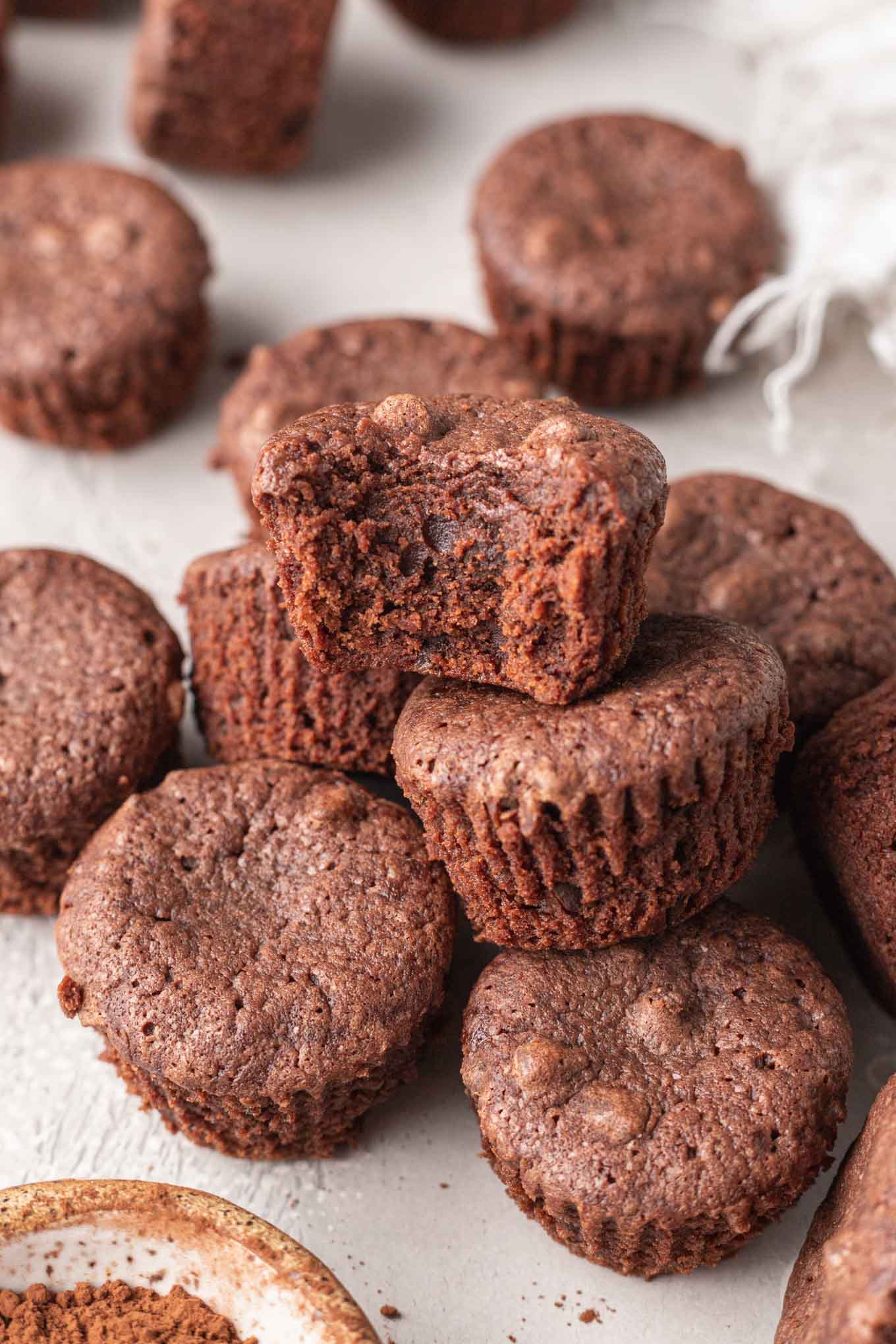 A bite-sized brownie with a bite missing, resting atop a pile of brownies. 