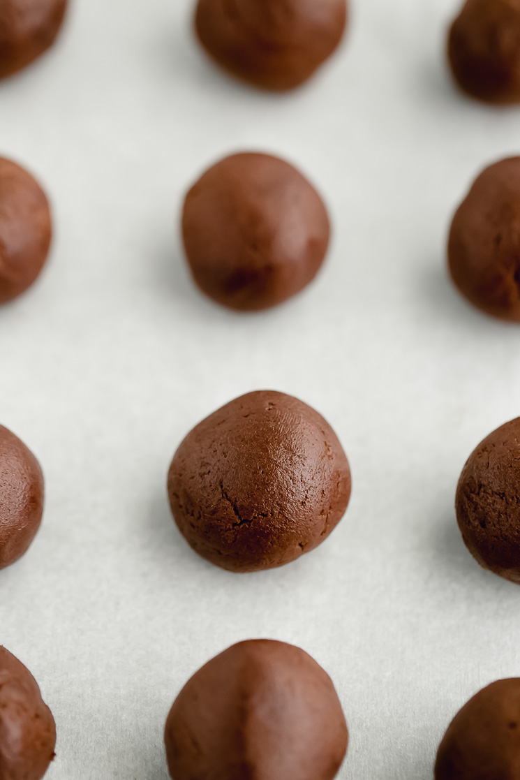 Cookie dough rolled into balls on top of a piece of parchment paper.