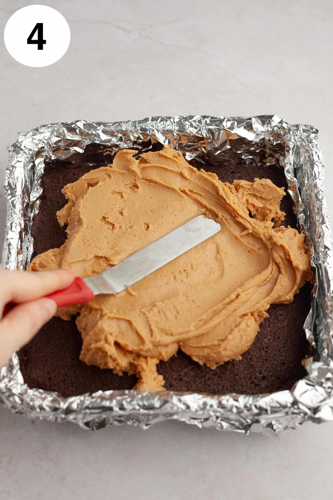 A process shot showing peanut butter fudge being smoothed onto brownies. 