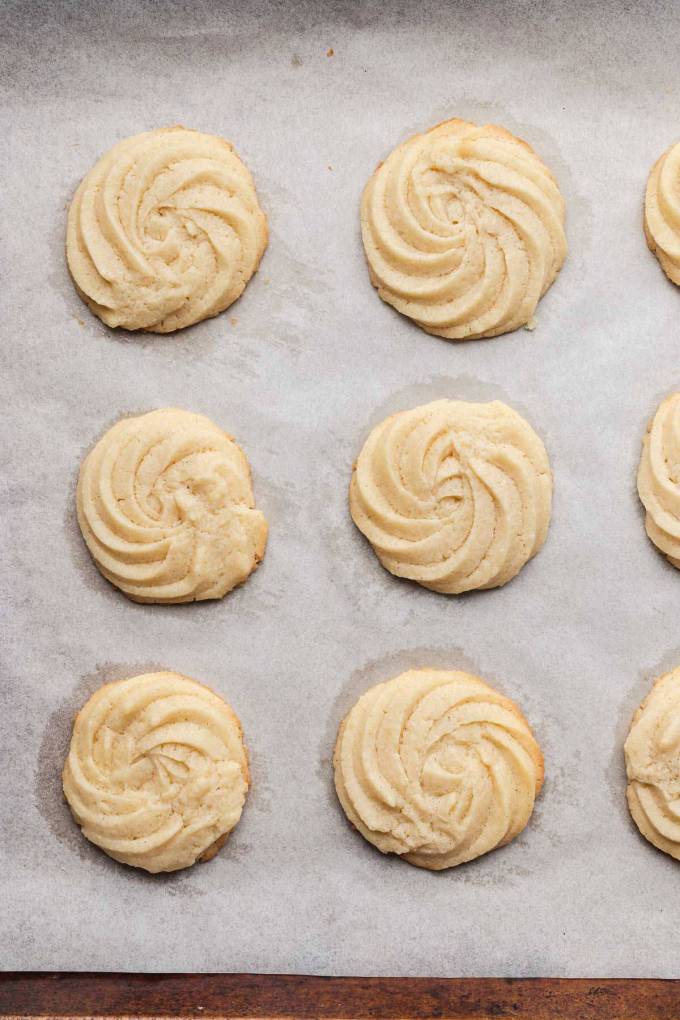 An overhead view of baked butter cookies on a parchment-lined baking sheet.