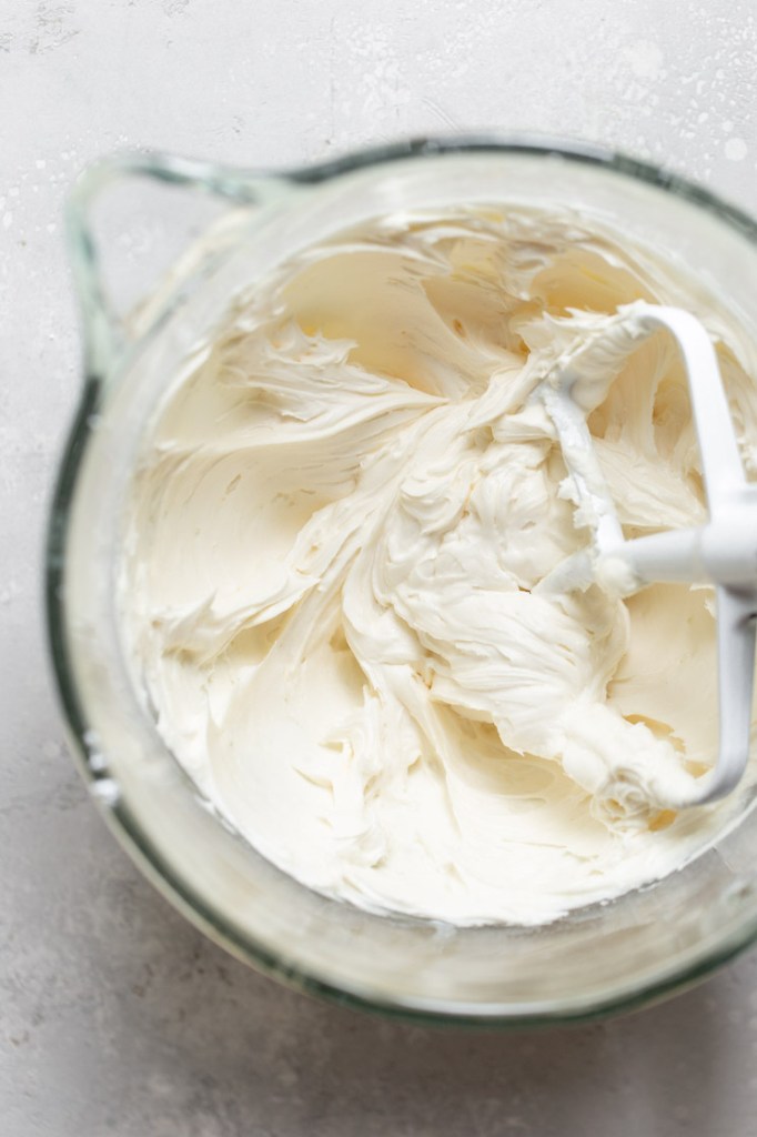 A glass mixing bowl holding a finished batch of buttercream frosting.