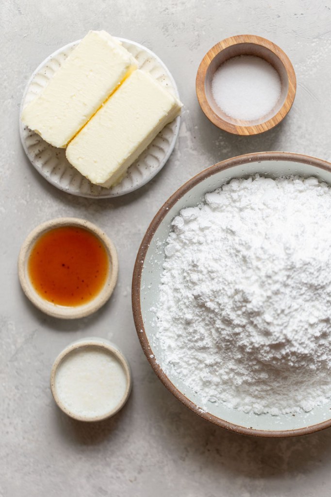 The ingredients needed to make a batch of buttercream frosting laid out in dishes on a gray surface.