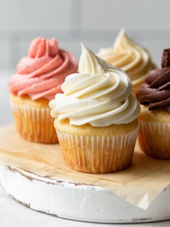 Four cupcakes topped with different flavors of buttercream frosting sitting on a rustic cake stand.