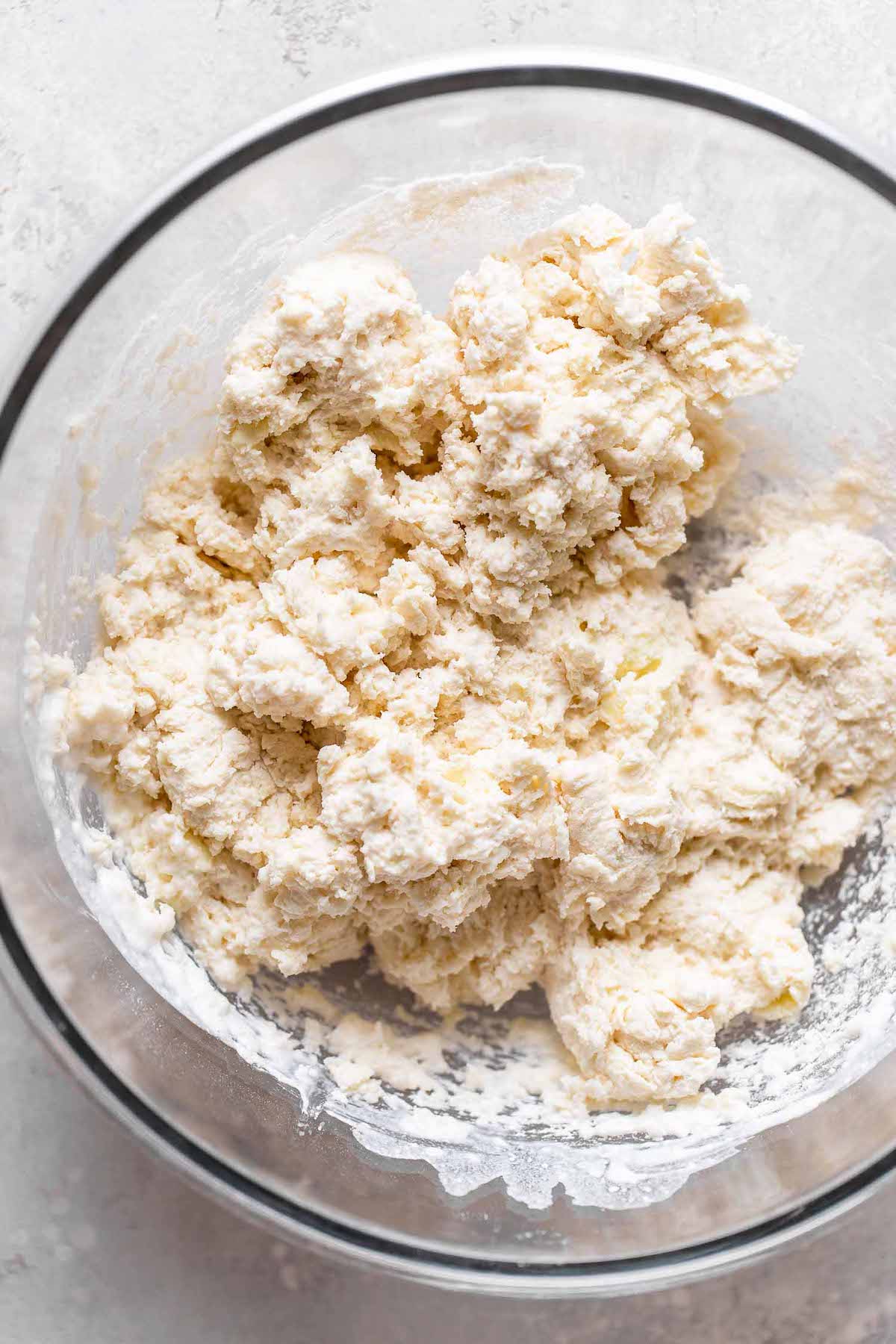 Overhead view of raw biscuit dough in a glass mixing bowl. 