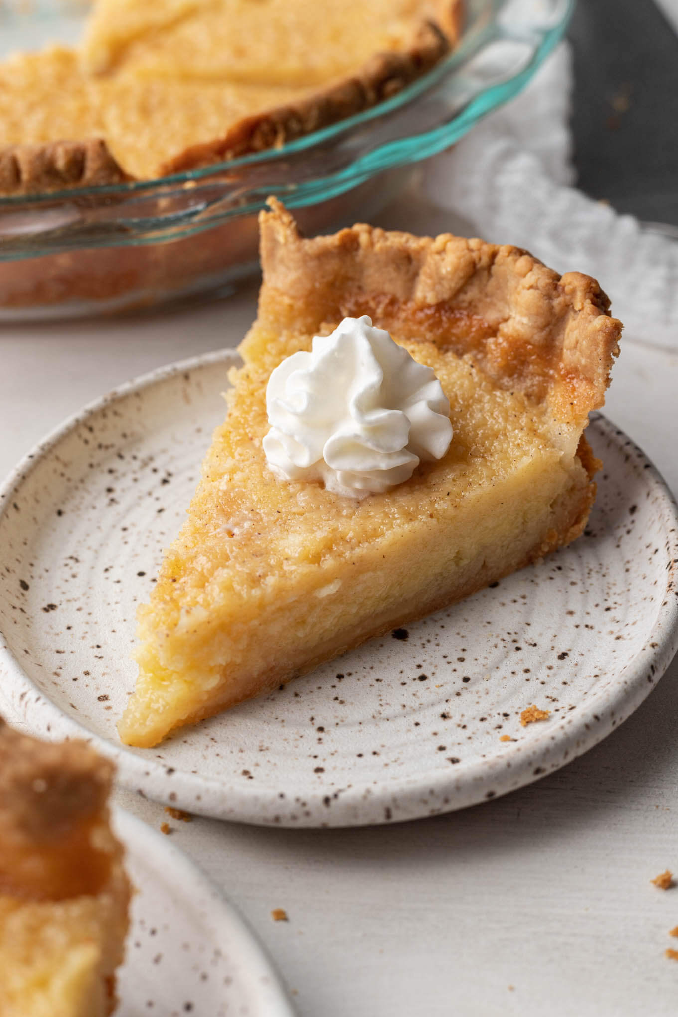 A slice of homemade buttermilk pie topped with whipped cream. 