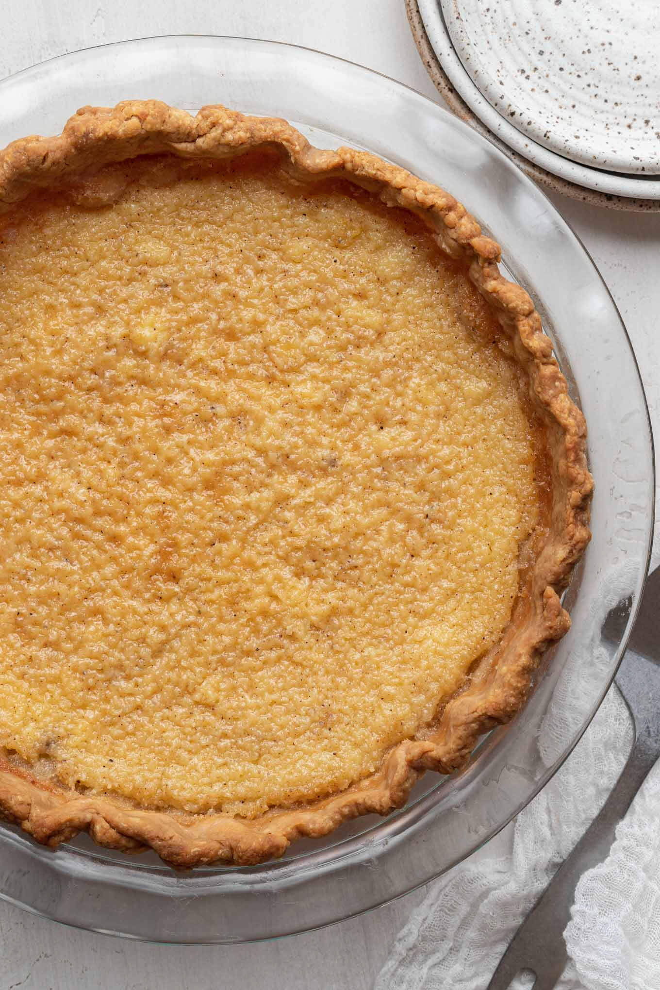 An overhead view of a baked buttermilk pie in a glass pie plate. 