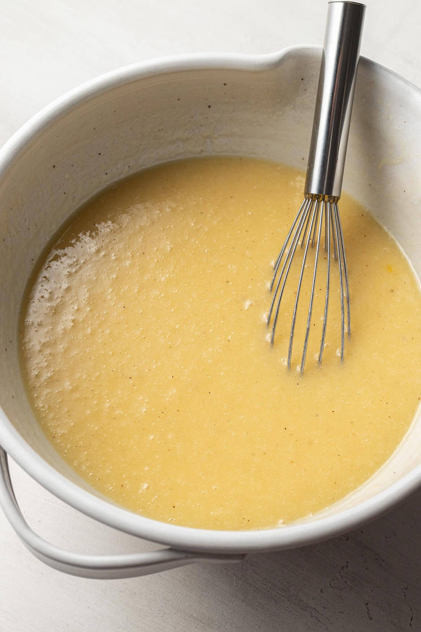 Buttermilk pie filling in a white mixing bowl with a wire whisk.