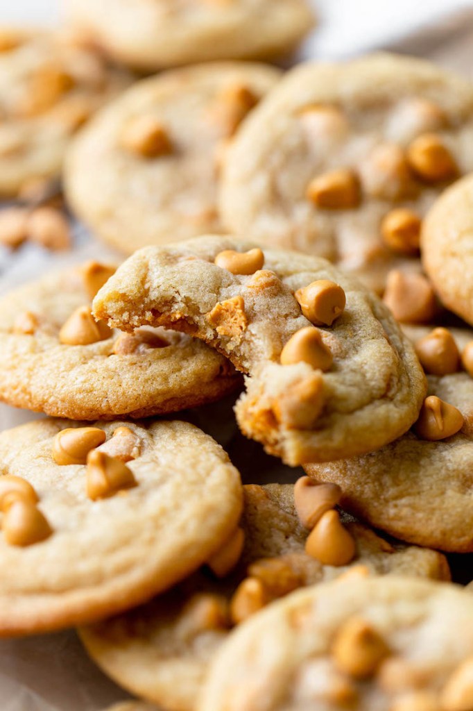 A pile of butterscotch chip cookies. The top cookie has a bite missing. 