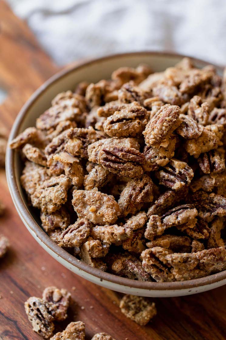 A rustic clay bowl filled with candied pecans resting on top of a wooden tray.