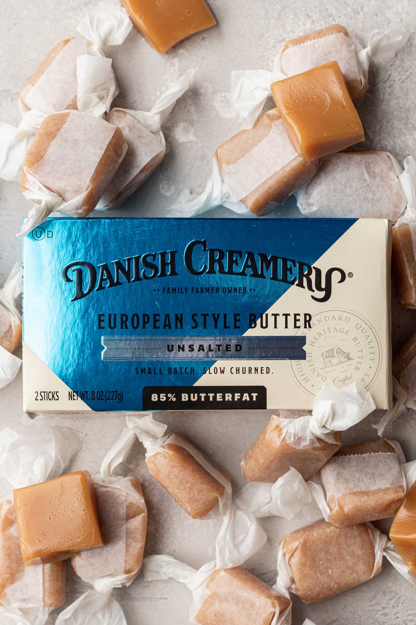 A container of Danish Creamery butter surrounded by homemade soft caramel candies. 