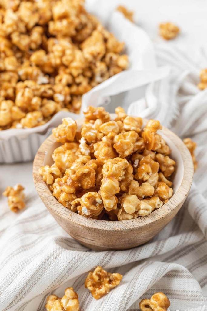 A close up view of a small bowl of homemade caramel corn. A larger bowl of popcorn rests in the background. 