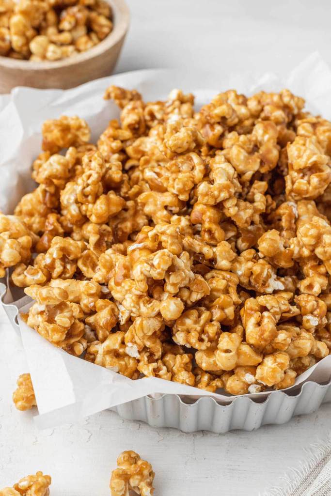 A metal tart pan piled high with homemade caramel corn. A smaller dish of popcorn rests in the background. 