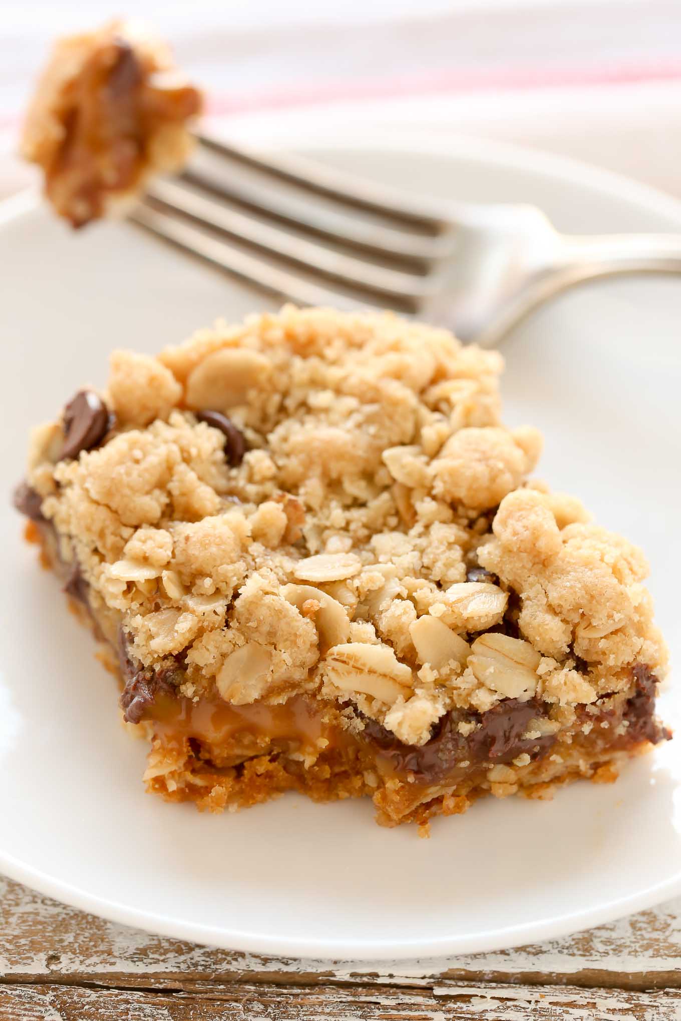 An oatmeal carmelita slice on a white plate. A fork rests on the plate. 