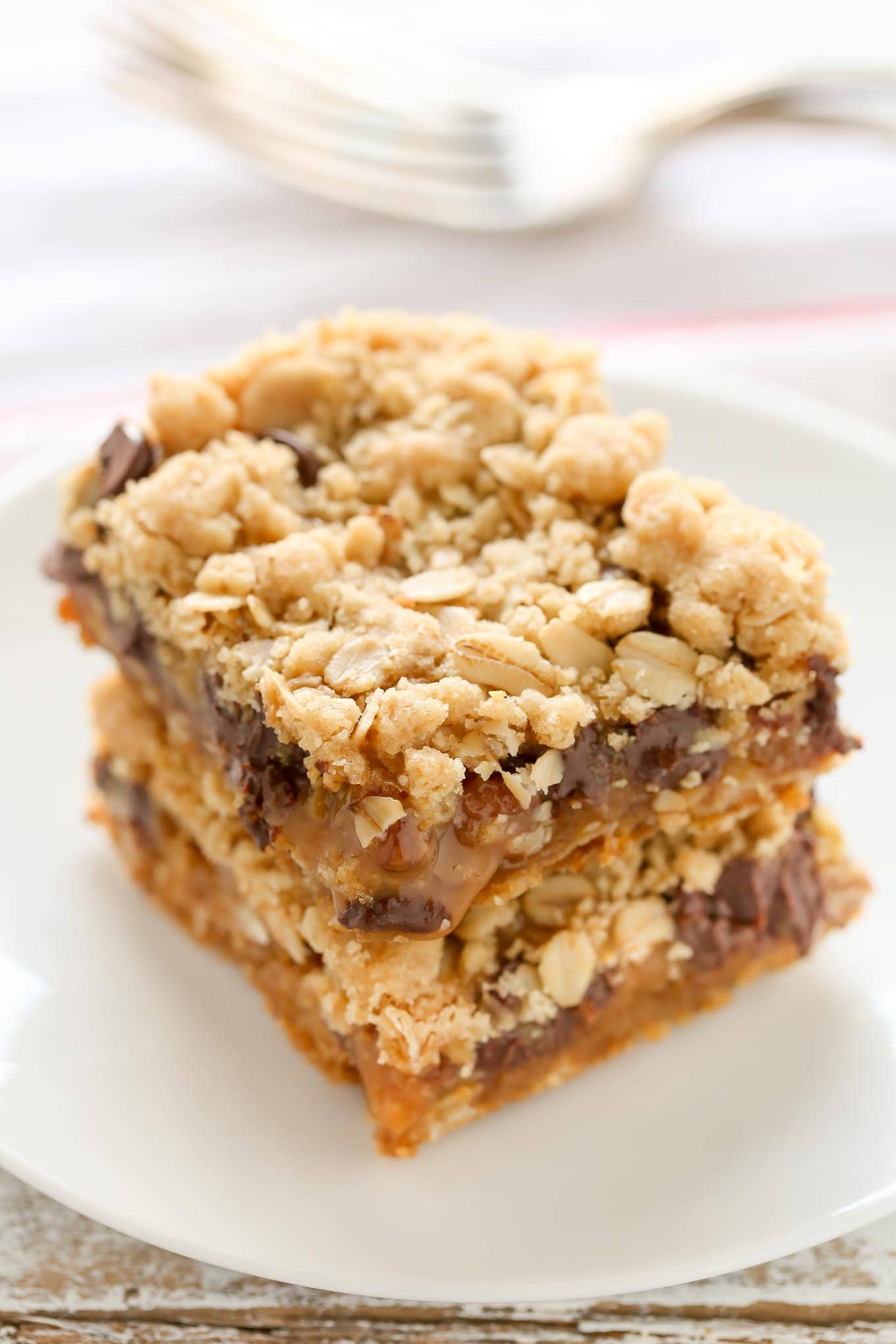 Two carmelitas stacked on a white plate. A fork rests on a tea towel in the background.