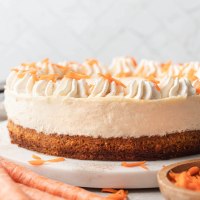 A carrot cake cheesecake topped with whipped cream on a marble serving platter.