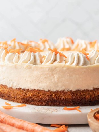 A carrot cake cheesecake topped with whipped cream on a marble serving platter.