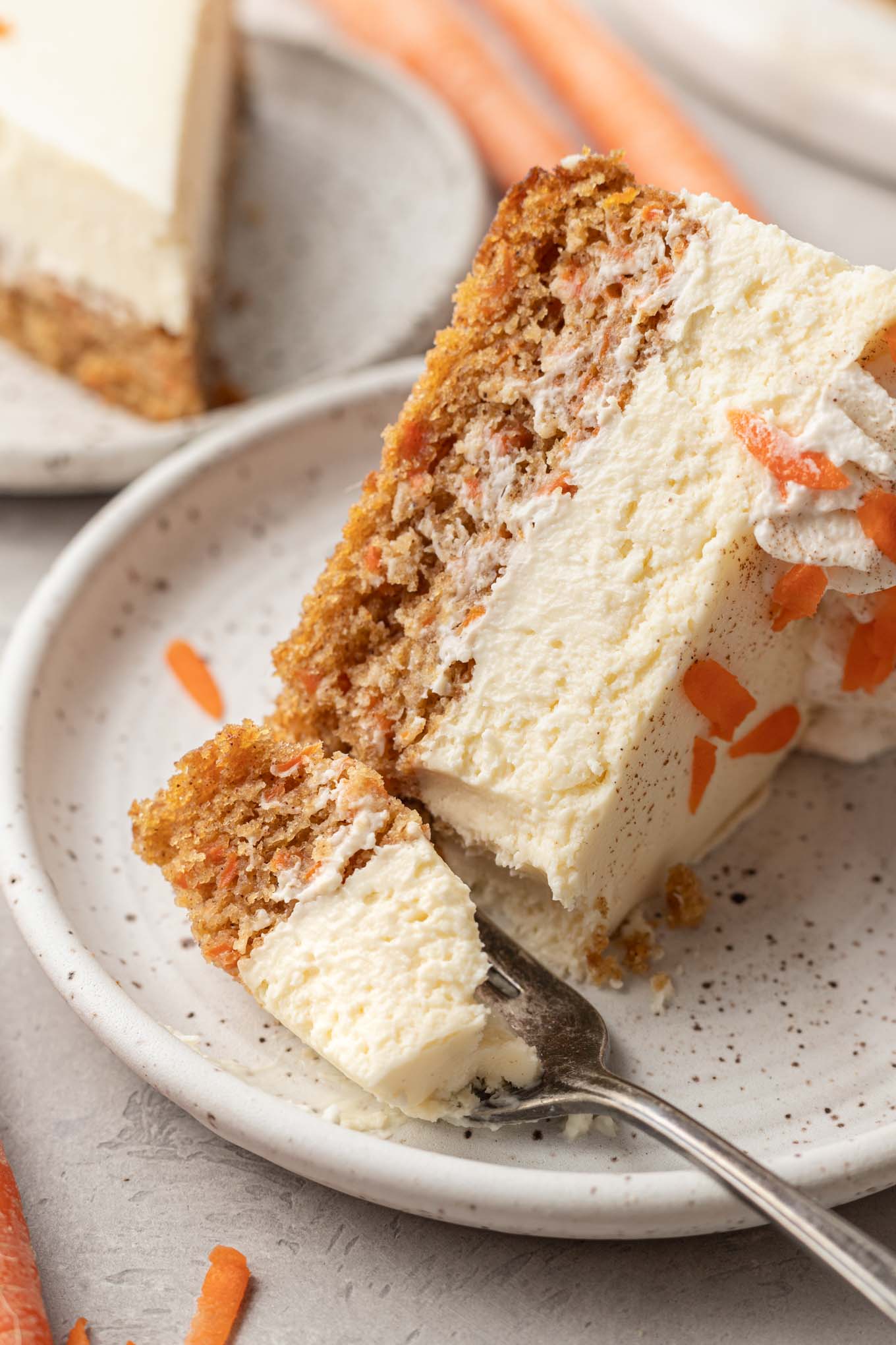 A slice of carrot cake cheesecake on a dessert plate with a fork. 