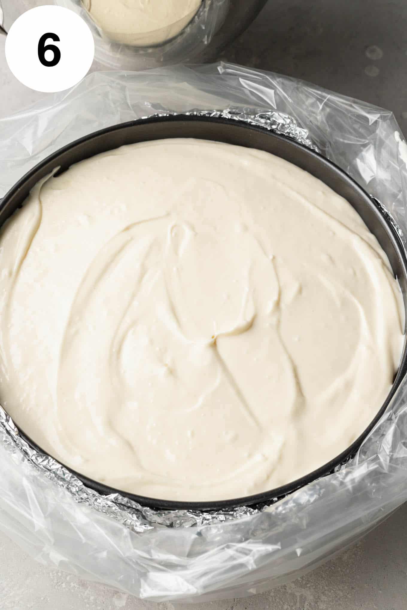 An overhead view of an unbaked cheesecake in a springform pan, wrapped in foil and an oven bag. 