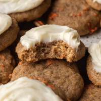 Several carrot cake cookies laying around each other. The top cookie has a bite missing.