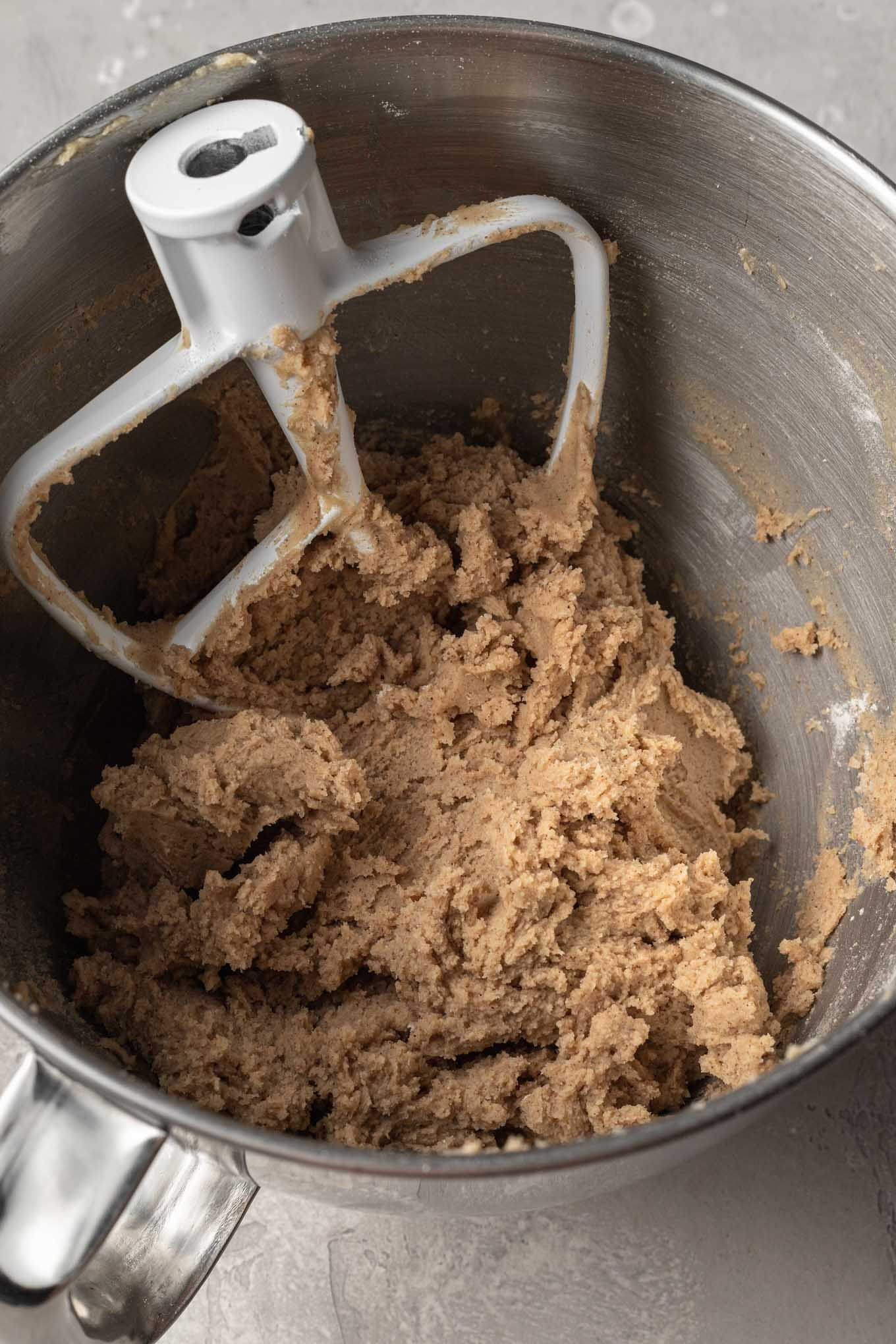 Carrot cake cookie dough in a metal mixing bowl, with a paddle attachment.