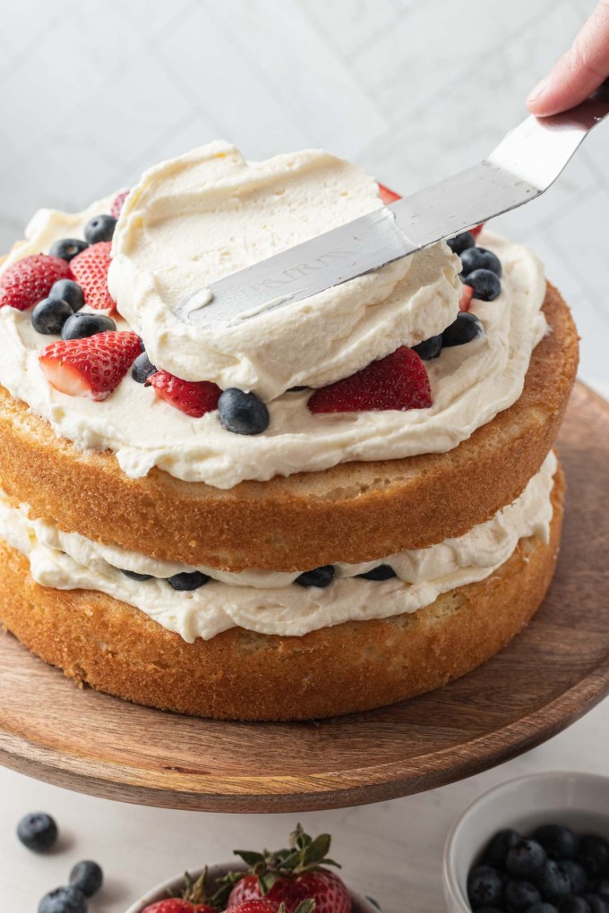 A process shot showing a chantilly berry cake being frosted.