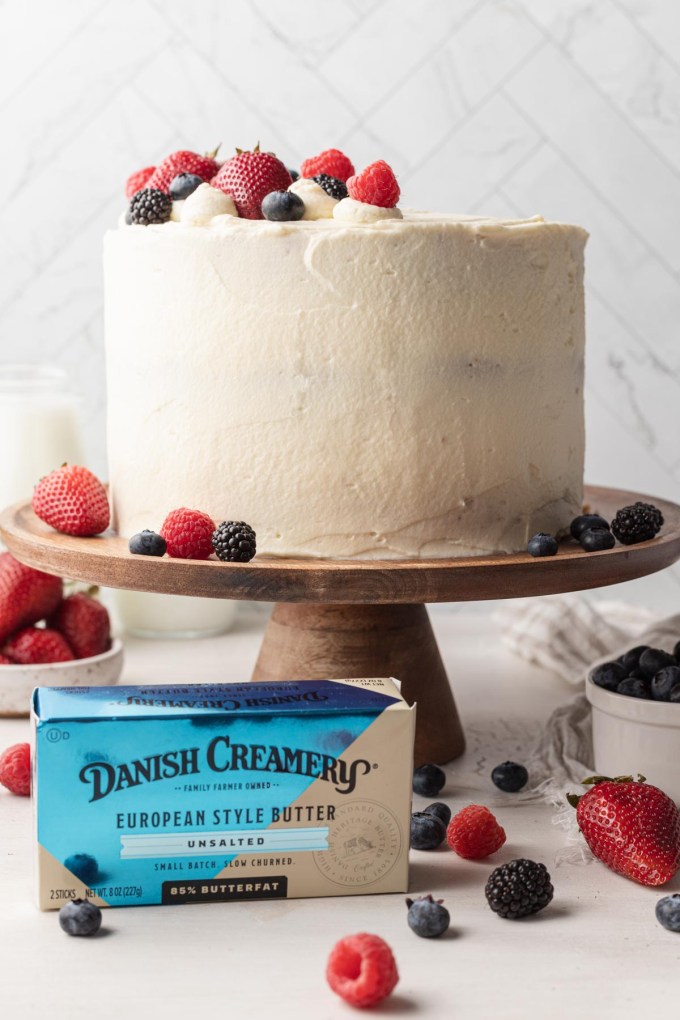 A Chantilly cake on a wooden cake stand, with a package of Danish Creamery butter in front of it. 