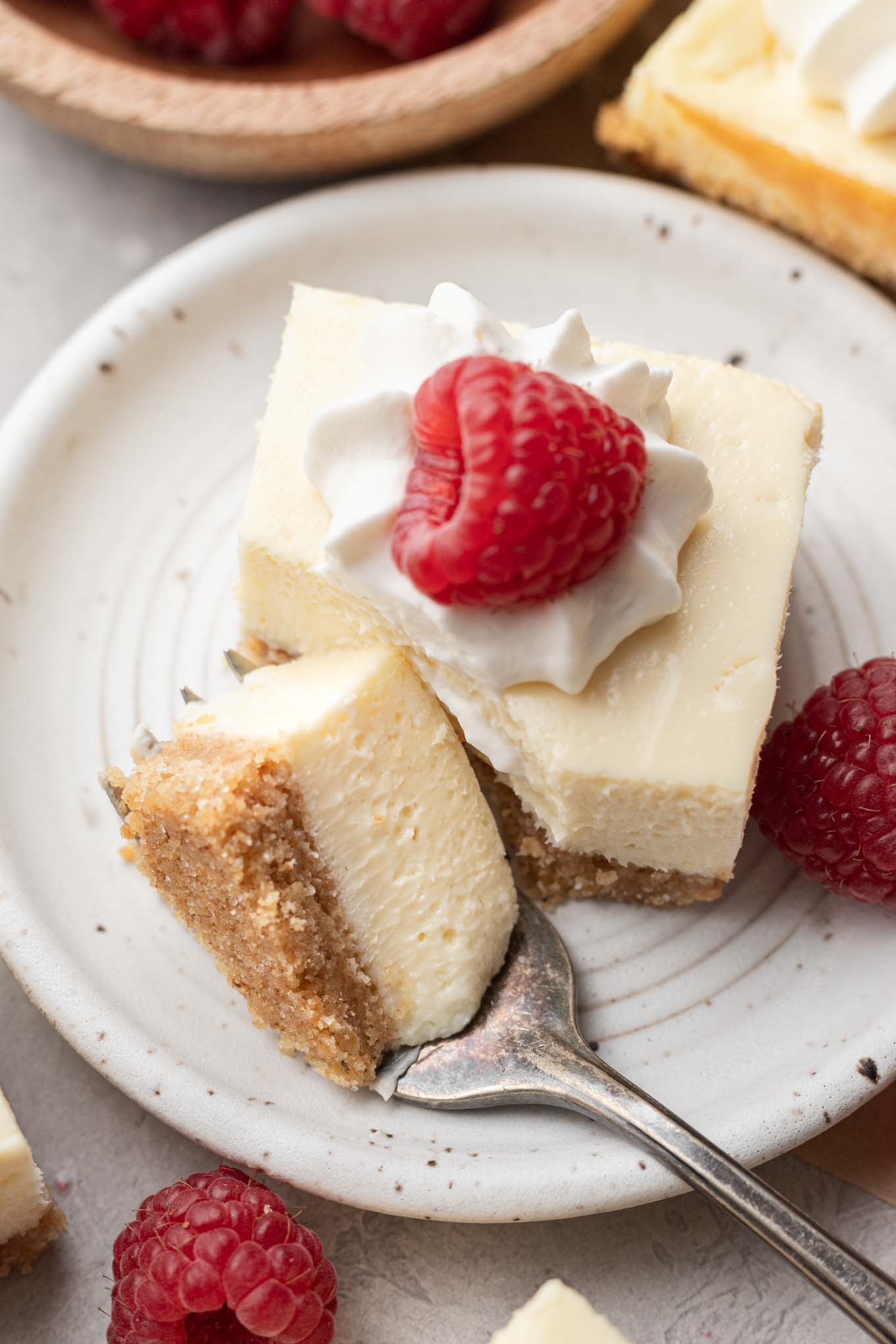 A close-up view of a cheesecake bar on a dessert plate. A piece has been carved off with a fork and rests on the plate. 