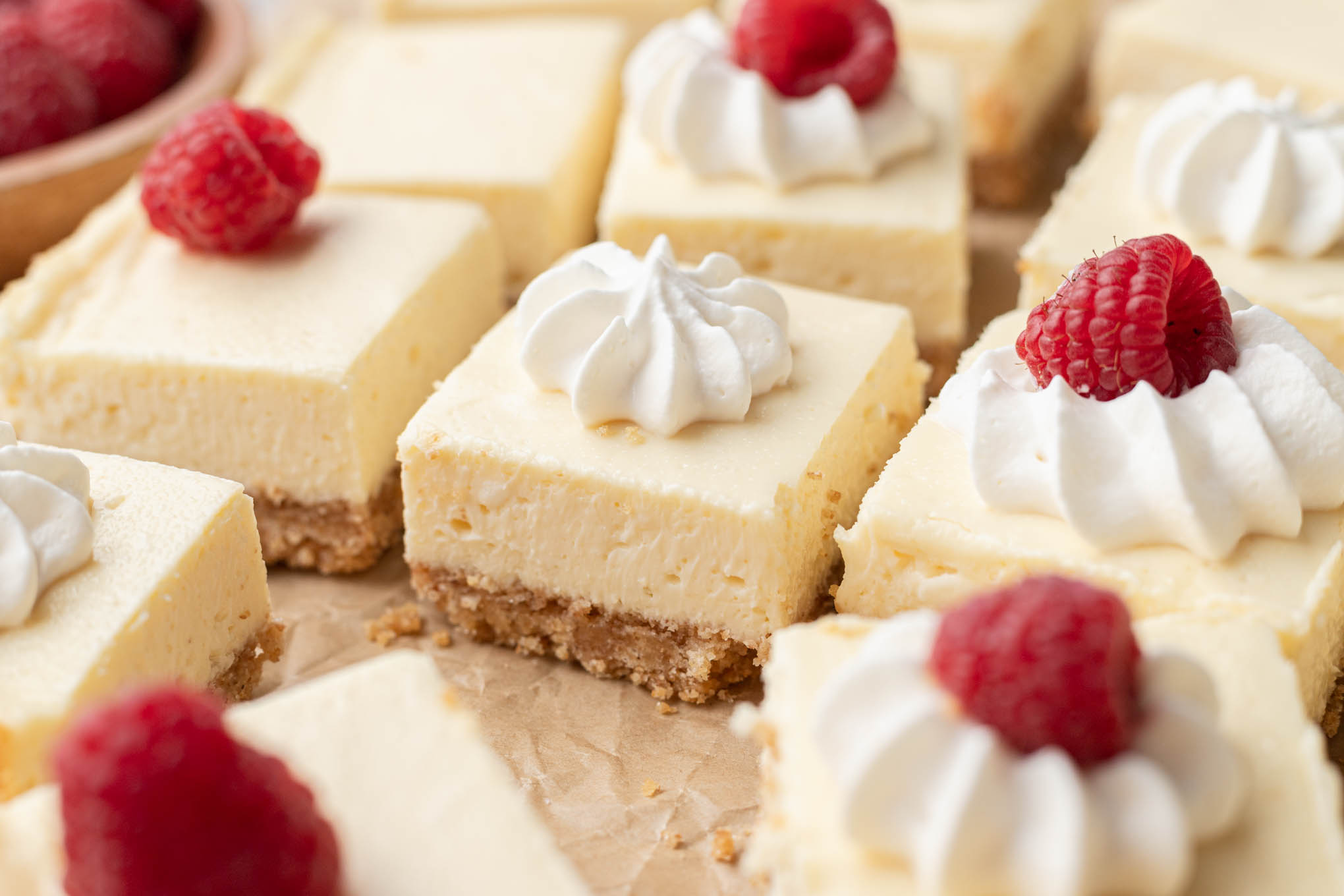 Several cheesecake bars topped with whipped cream and a fresh raspberry.