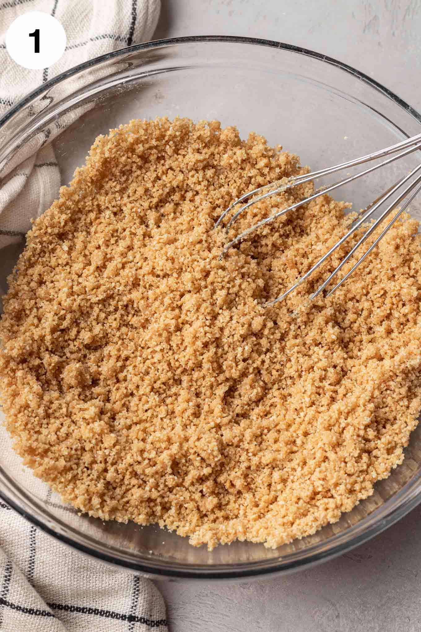 An overhead view of the graham cracker mixture in a glass mixing bowl. 