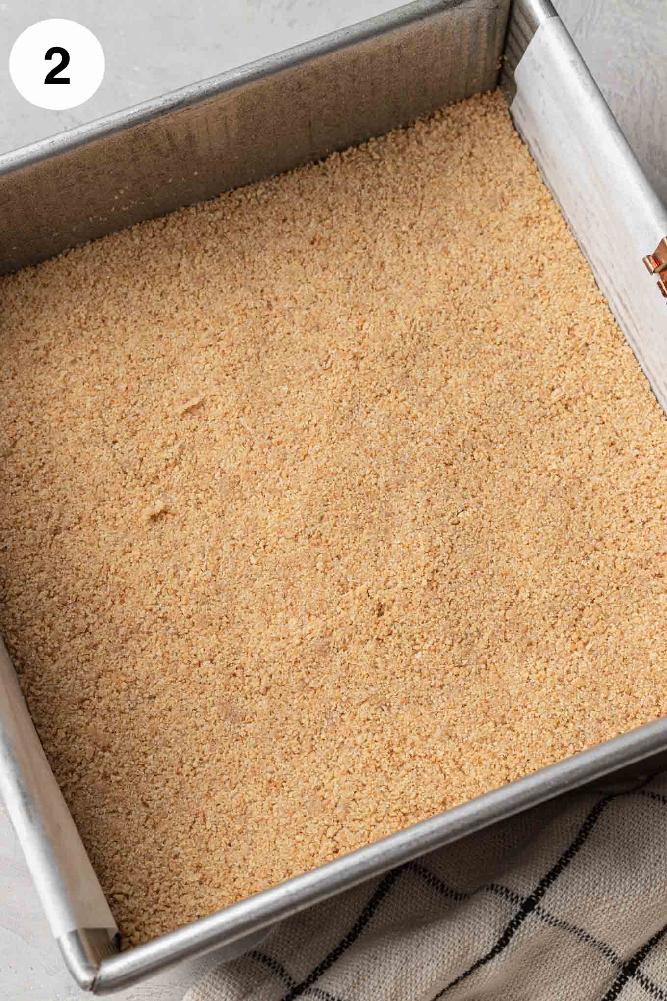 An overhead view of a graham cracker crust in an 8-inch square baking dish. 