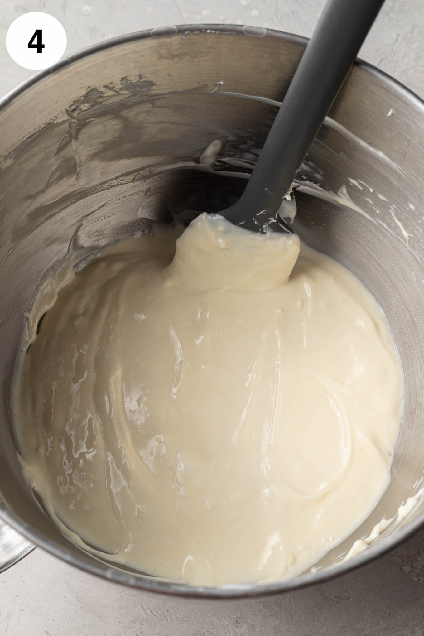 An overhead view of cheesecake filling in the bowl of a stand mixer, with a rubber spatula. 