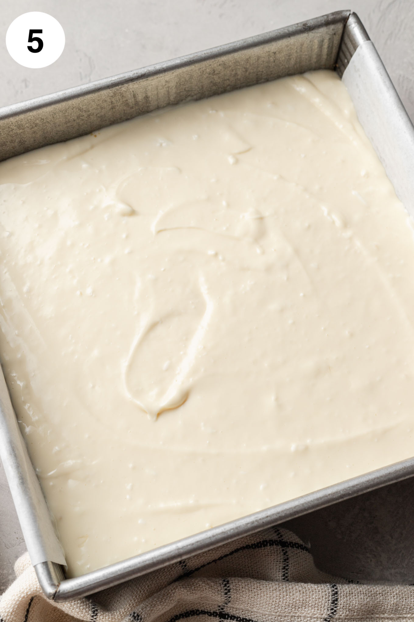 An overhead view of unbaked cheesecake bars in a square baking dish. 