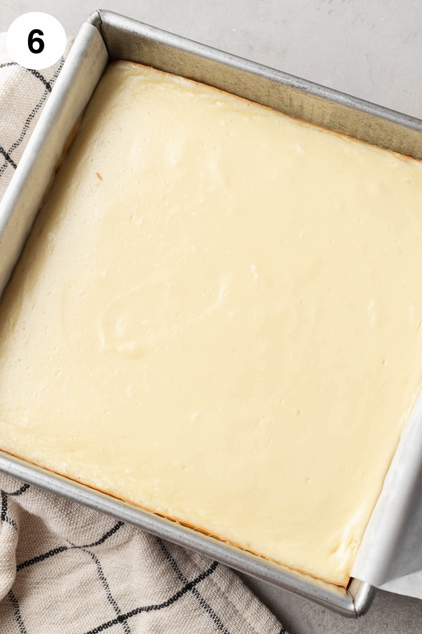 An overhead view of baked cheesecake bars in a square baking dish. 